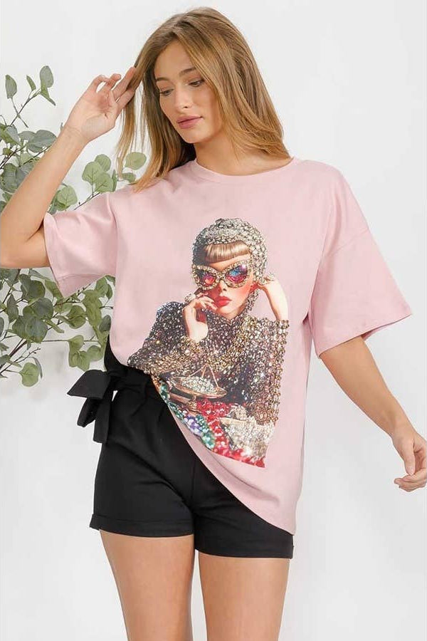 Woman wearing a pink t-shirt with a graphic design, standing against a white background. Born To Glam