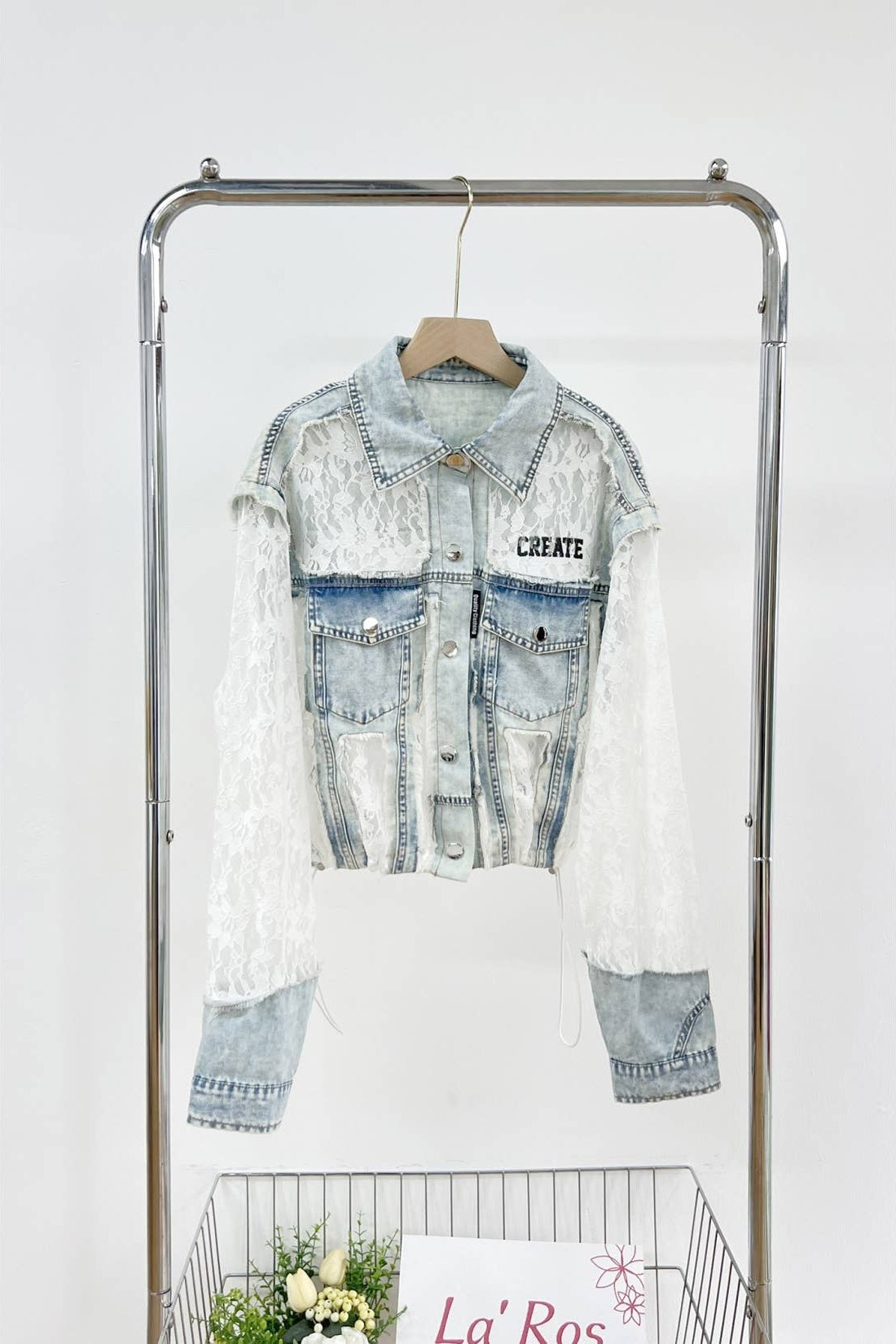 Denim jacket with lace overlay on a clothing rack against a white background Born To Glam