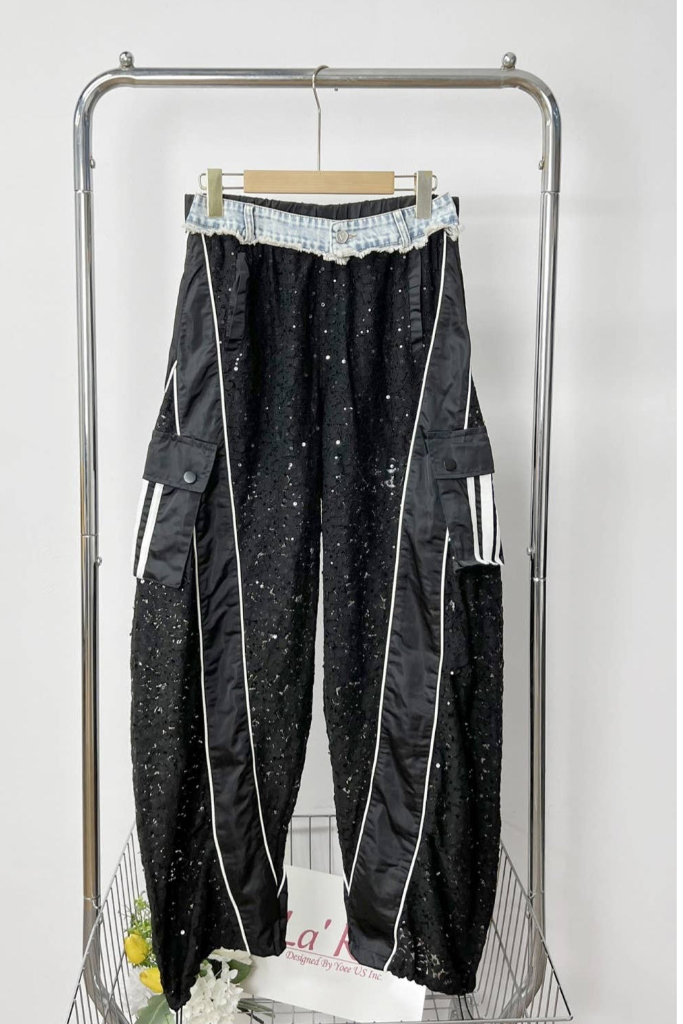 Black pants with white accents hanging on a rack against a white background Born To Glam