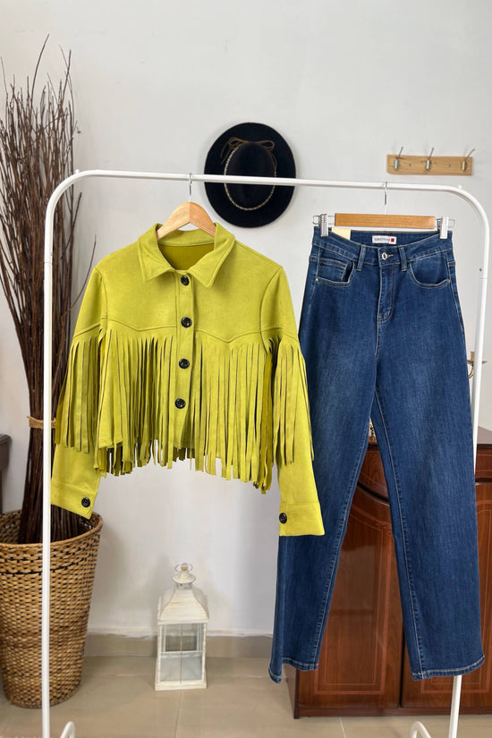 Yellow fringed jacket and blue jeans on a white rack against a neutral wall. Born To Glam