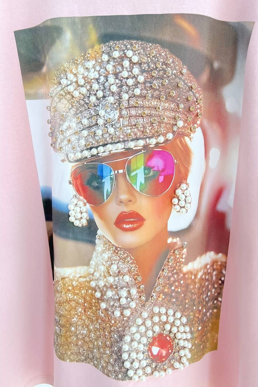 Person wearing a sparkling outfit with a hat and sunglasses on a pink background Born To Glam