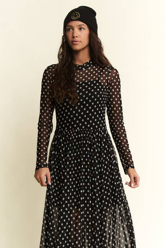 Woman wearing a black polka dot dress with long sleeves on a beige background Born To Glam