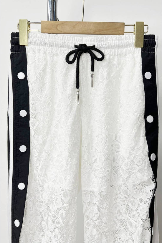 White lace pants with black polka dot straps on a hanger against a white background Born To Glam