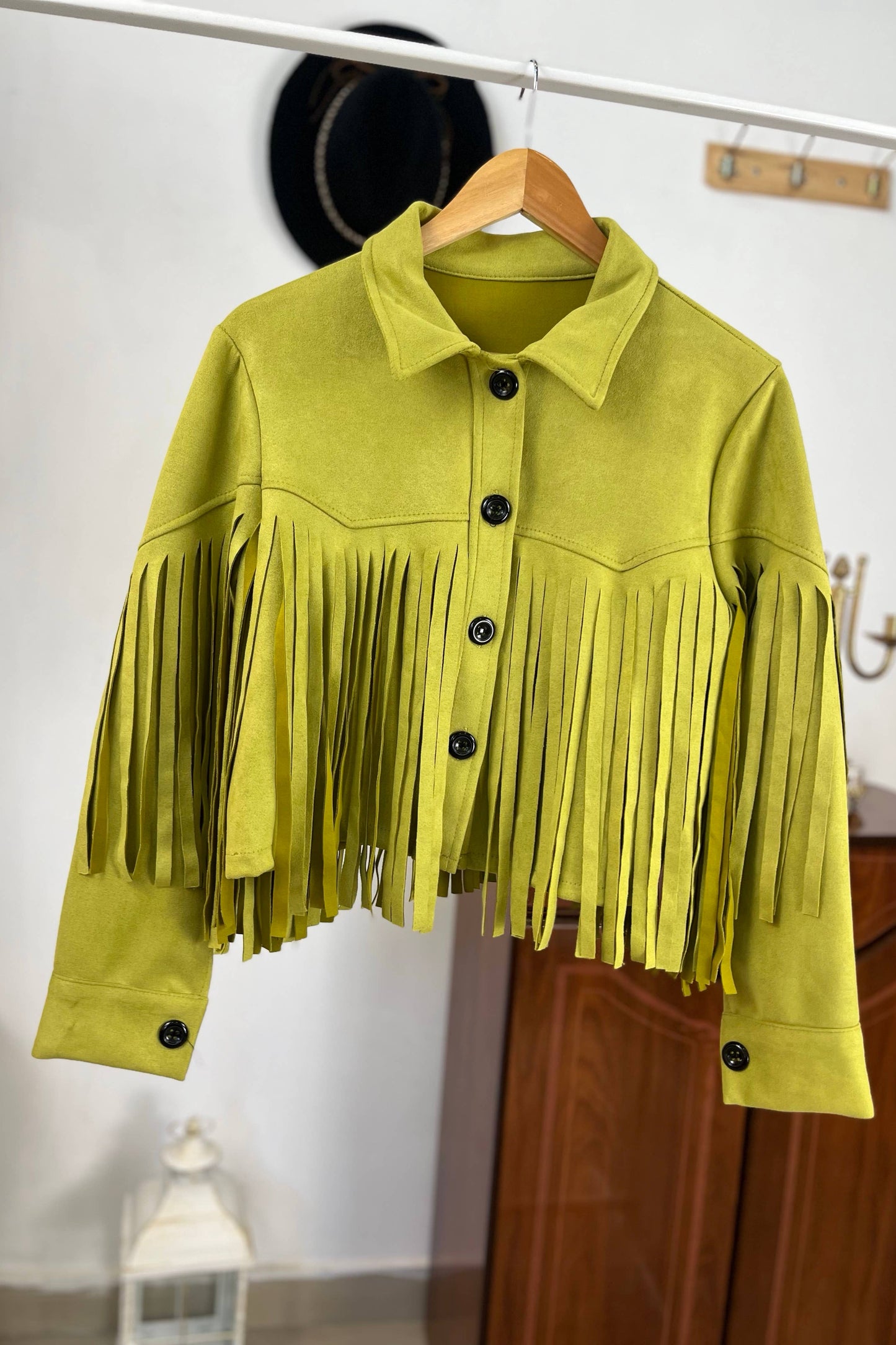 Yellow fringed jacket on a hanger against a white wall. Born To Glam