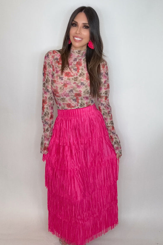 Woman wearing a floral top and pink fringe skirt against a white background Born To Glam