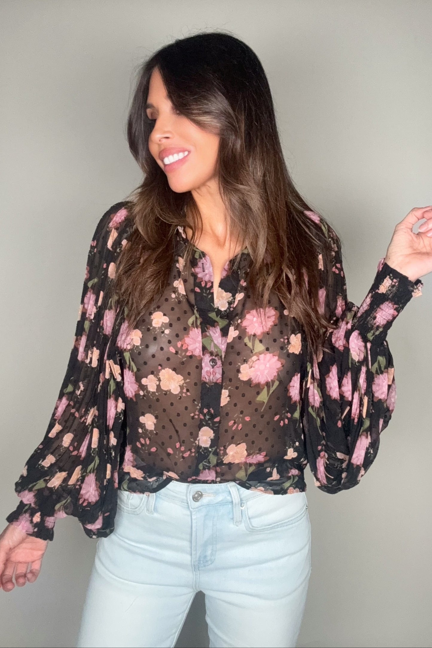 Woman wearing a floral blouse with sheer sleeves against a plain background Born To Glam