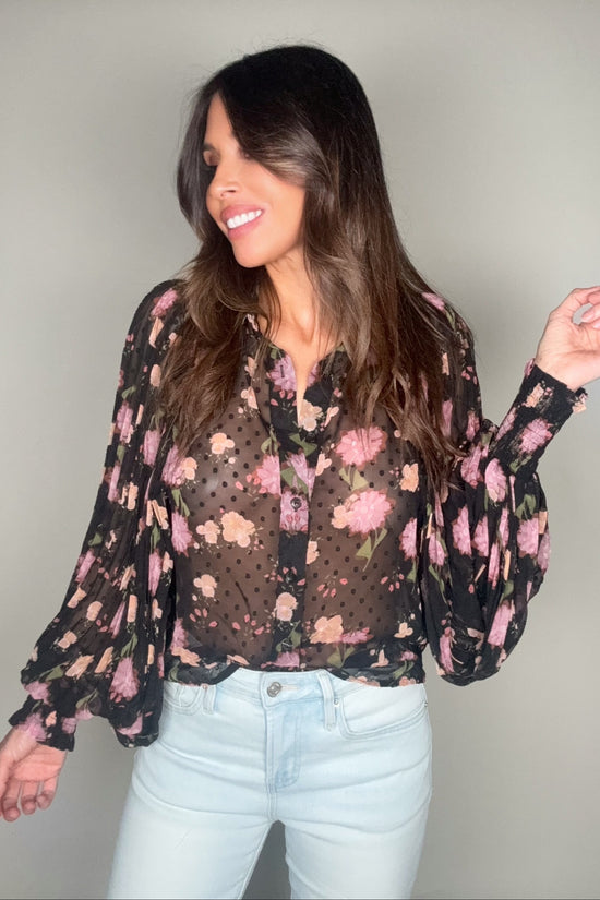 Woman wearing a floral blouse with sheer sleeves against a plain background Born To Glam