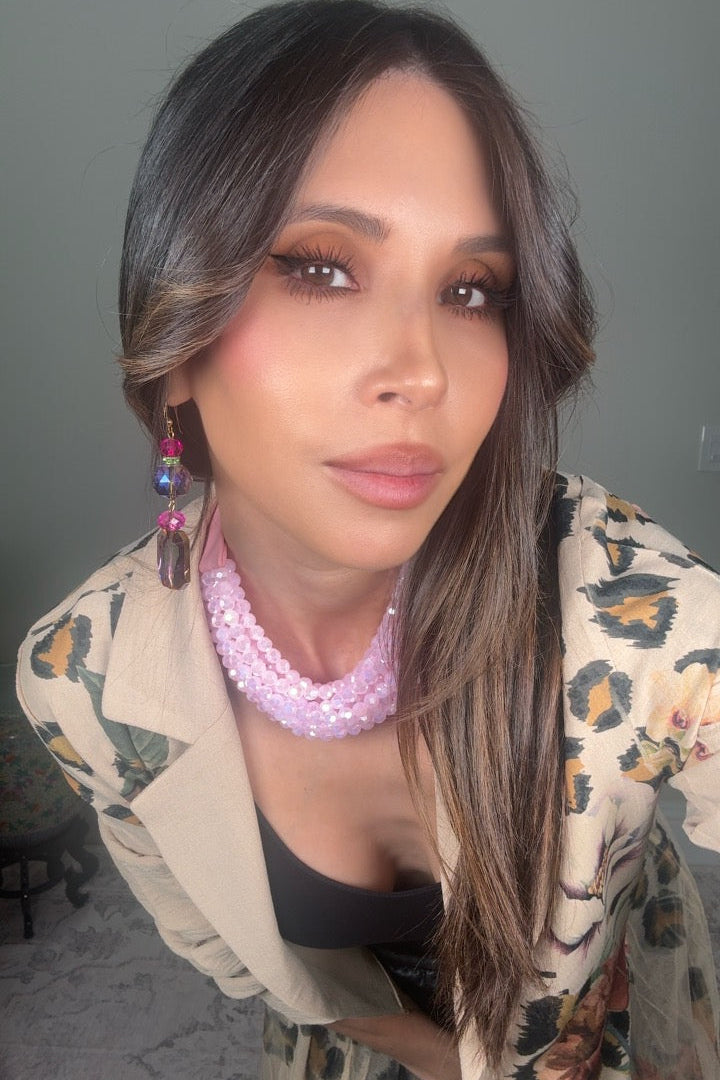 Woman wearing a floral jacket and colorful jewelry against a neutral background Born To Glam