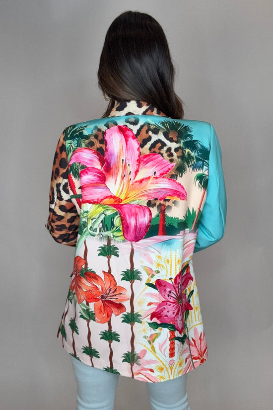 Person wearing a colorful floral and leopard print headscarf on a plain background Born To Glam