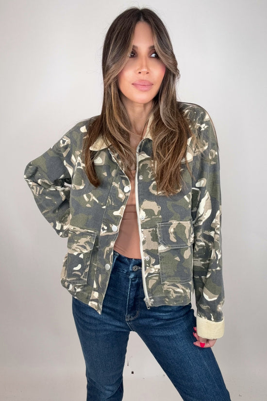 Woman wearing a camouflage jacket and blue jeans against a plain background Born To Glam