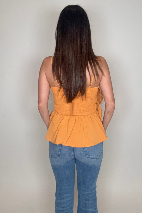Person wearing an orange top and blue jeans on a plain background Born To Glam