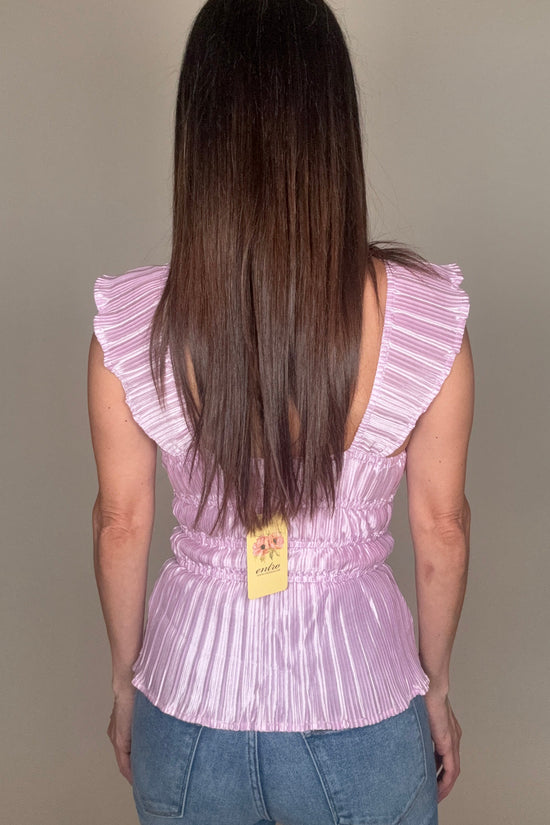 Person wearing a pink pleated top and blue jeans on a plain background Born To Glam