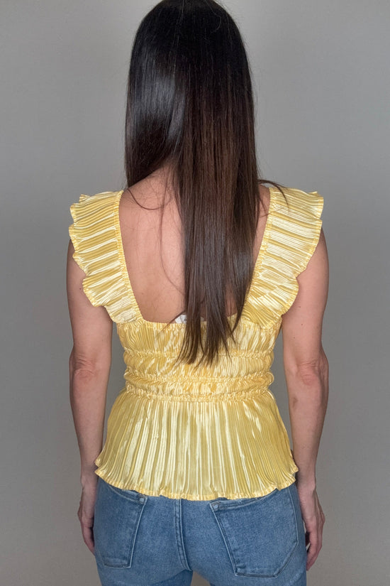 Person wearing a yellow pleated top and blue jeans on a gray background Born To Glam