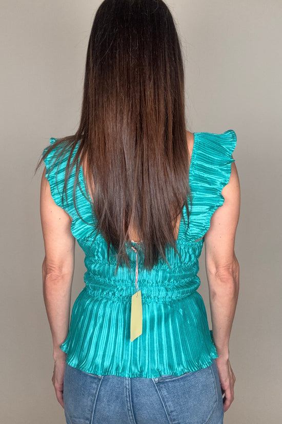 Person wearing a teal dress with ruffled shoulders against a plain background Born To Glam