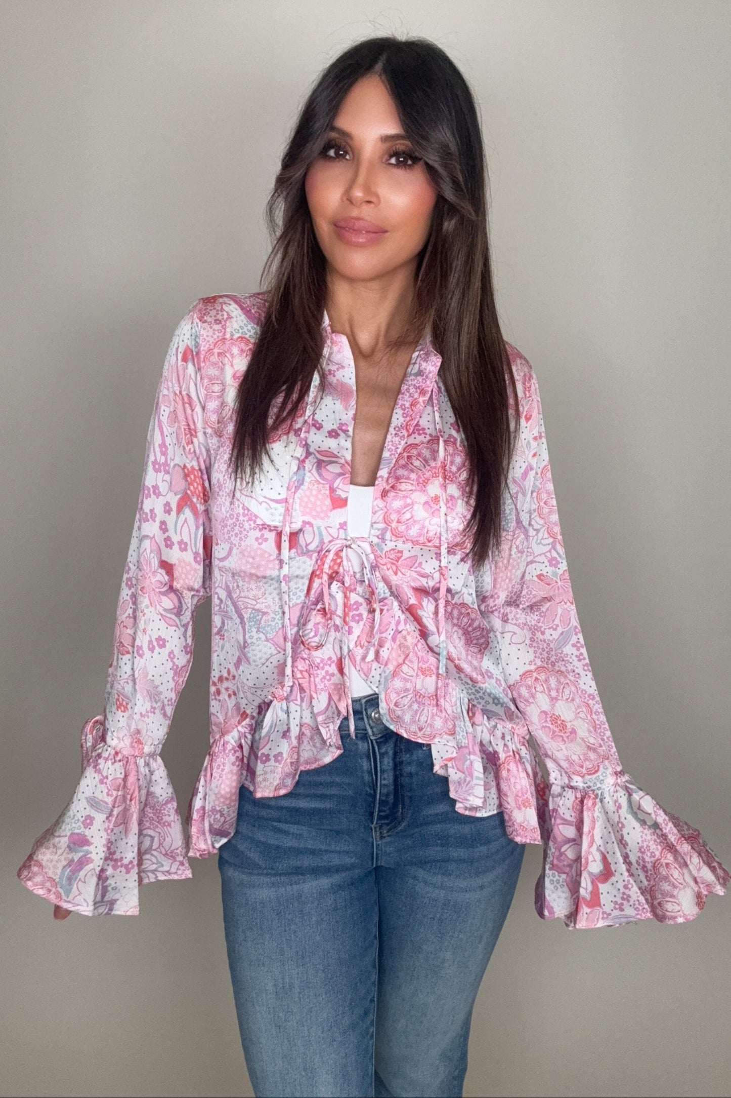 Woman wearing a pink floral blouse with ruffled sleeves against a plain background Born To Glam