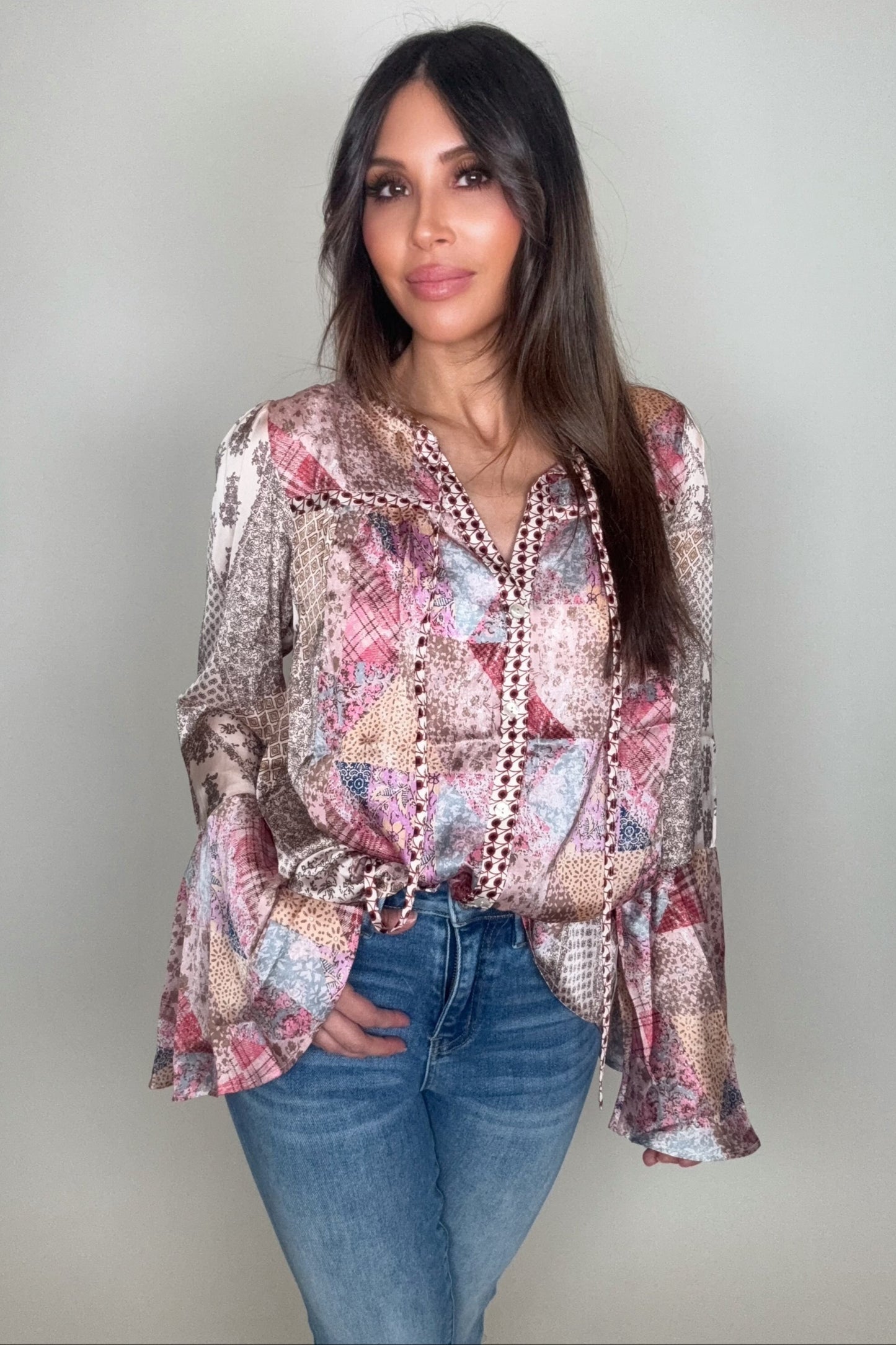 Woman wearing a patterned blouse and jeans against a plain background Born To Glam