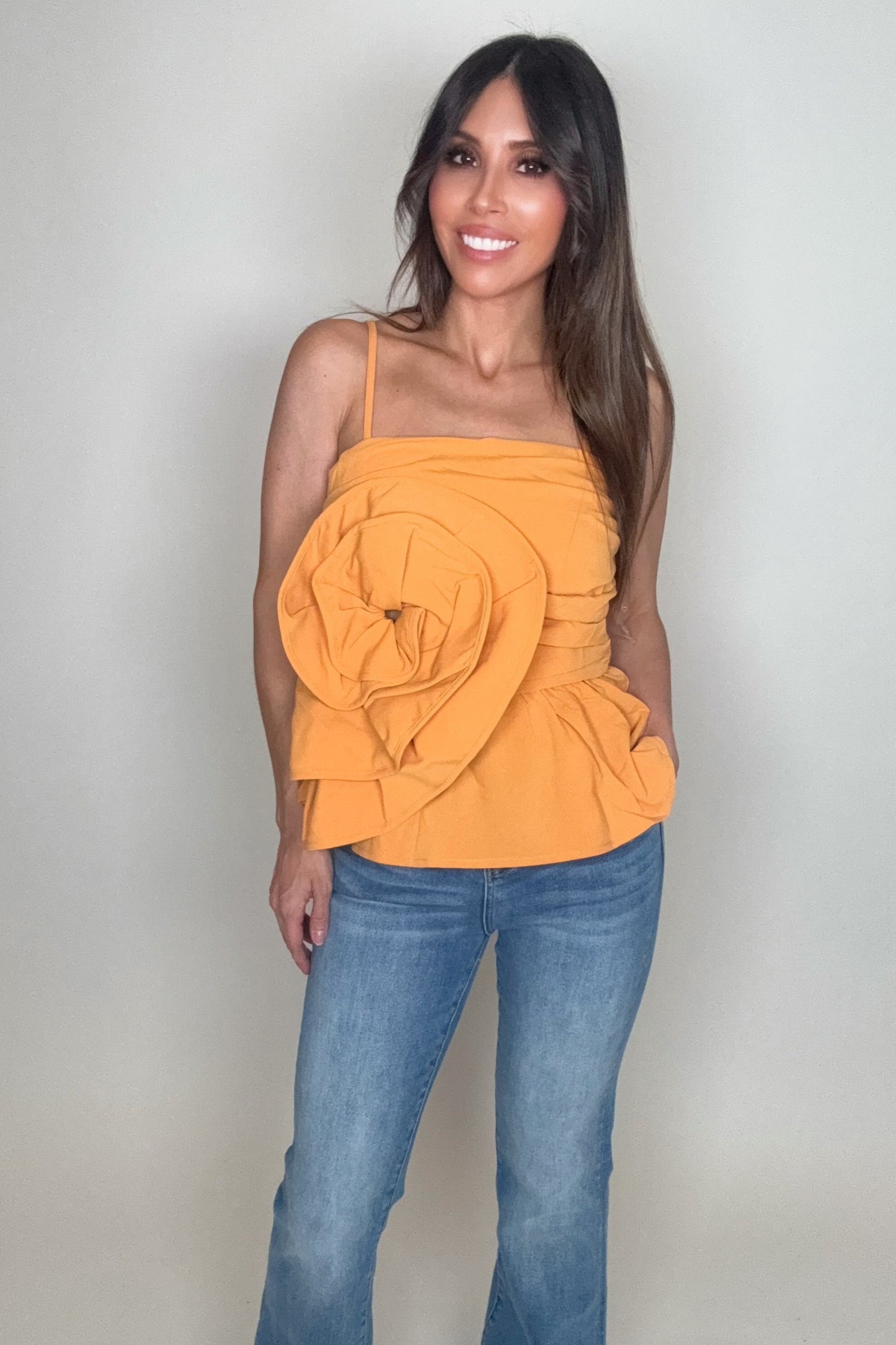 Woman wearing an orange top and blue jeans against a plain background Born To Glam