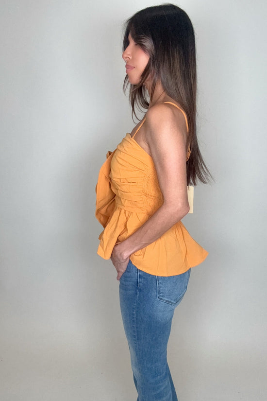 Woman wearing a mustard yellow top and blue jeans against a plain background Born To Glam
