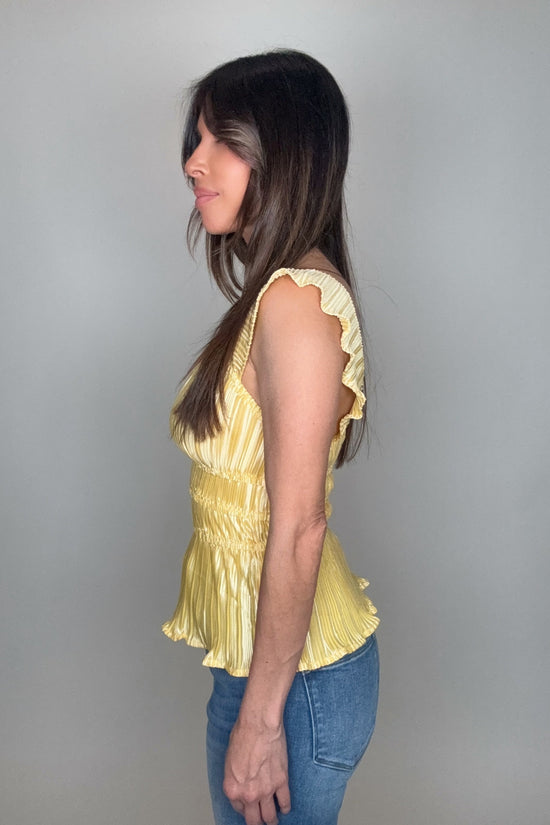 Woman wearing a yellow top and blue jeans against a gray background Born To Glam
