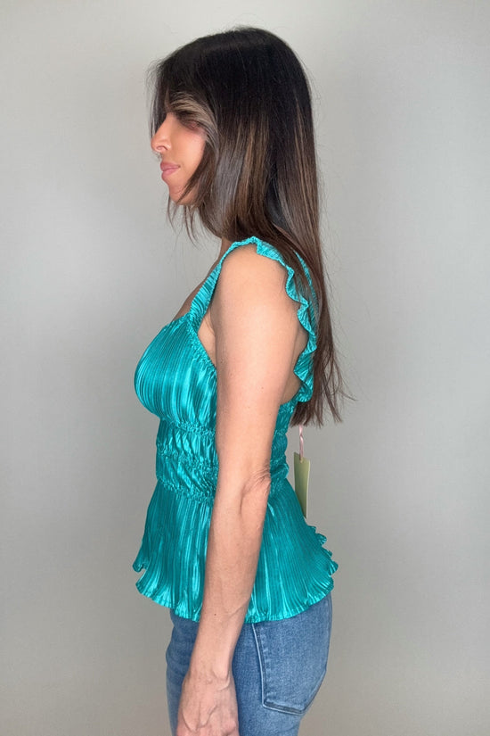 Woman wearing a teal top with ruffled details against a plain background Born To Glam