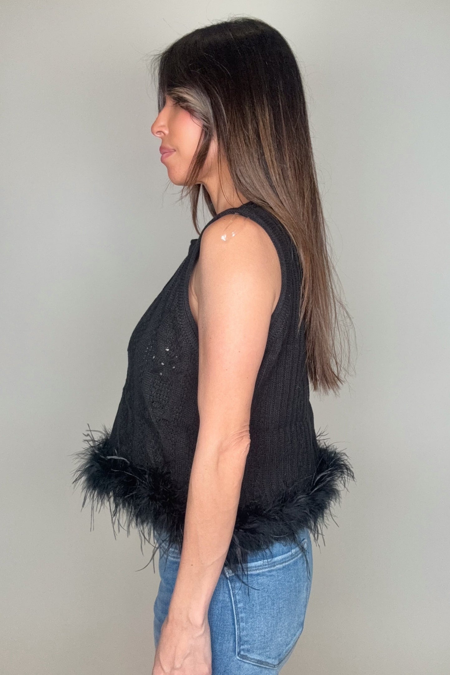 Woman wearing a black sleeveless top with feather details on a plain background Born To Glam