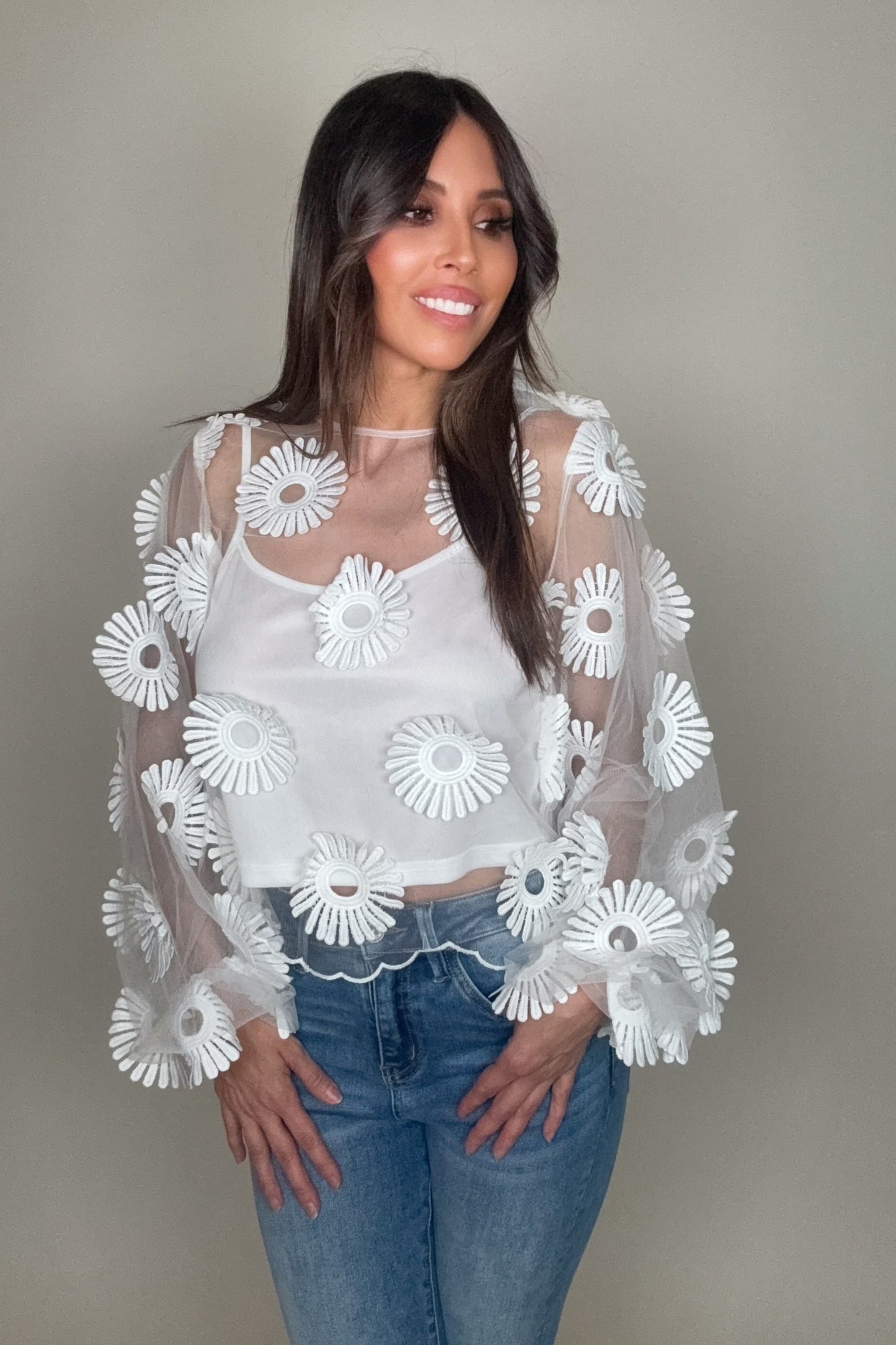 Woman wearing a sheer top with white floral embroidery against a plain background Born To Glam