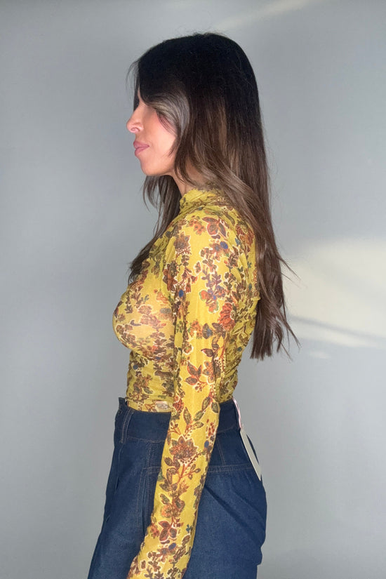 Person wearing a yellow floral jacket and blue jeans against a plain background Born To Glam