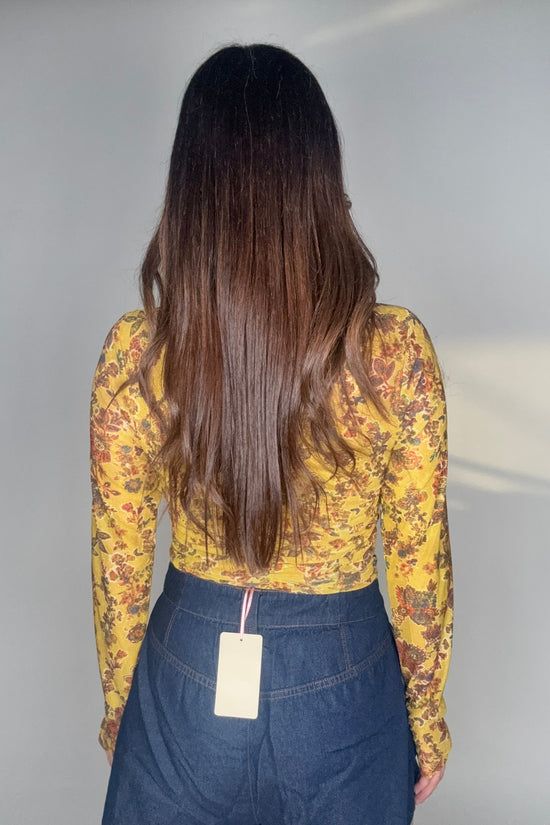 Person wearing a yellow floral top and blue jeans on a plain background Born To Glam