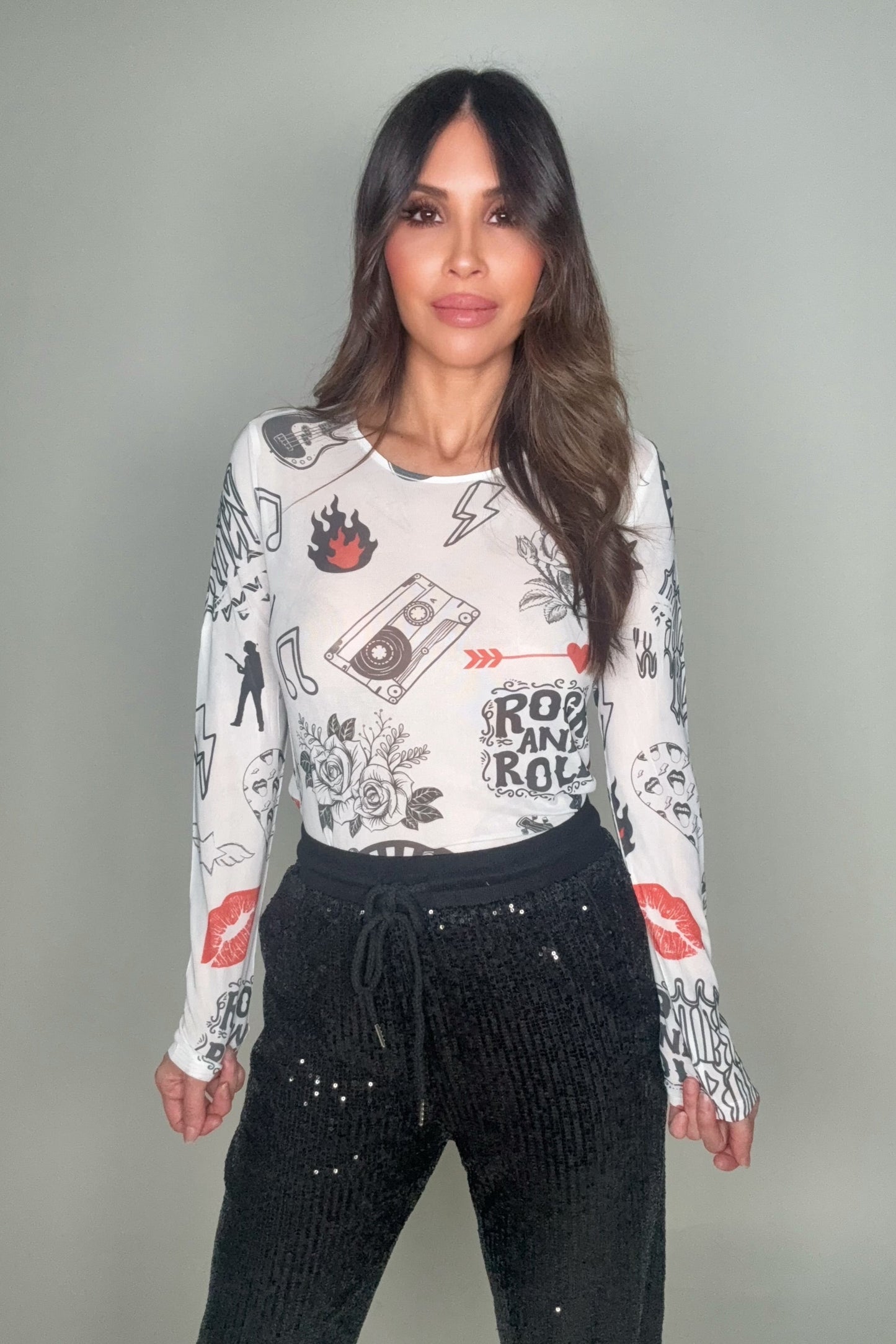 Woman wearing a long-sleeve graphic shirt and black pants against a gray background Born To Glam