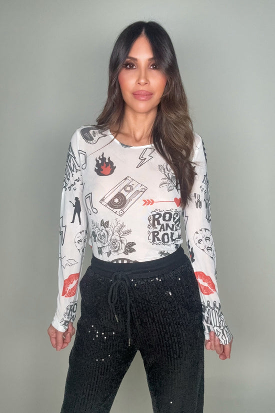 Woman wearing a long-sleeve graphic shirt and black pants against a gray background Born To Glam