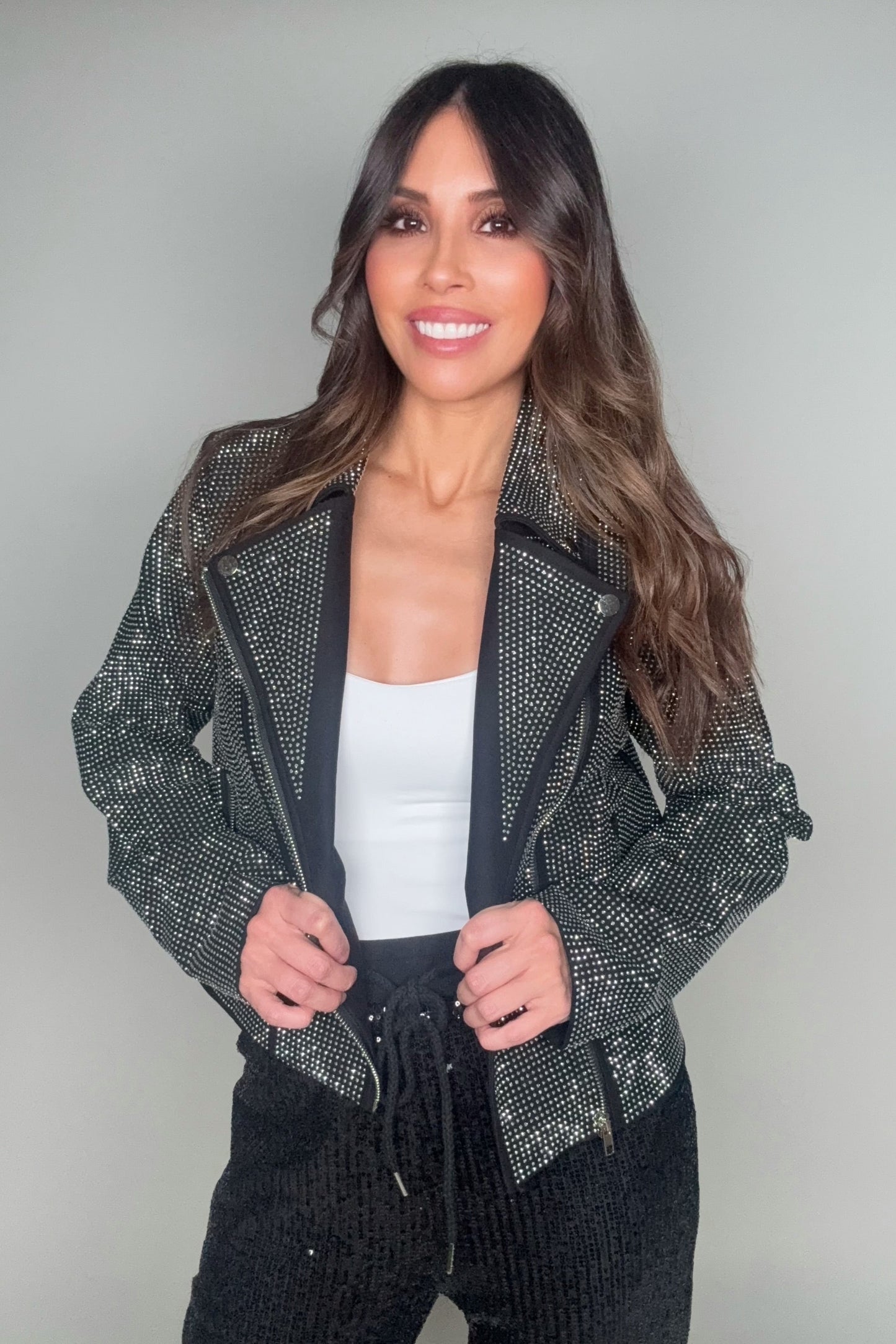 Woman wearing a black sequin jacket over a white top and black pants on a gray background Born To Glam