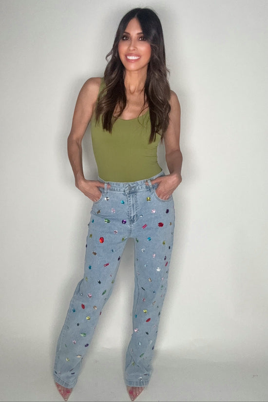 Woman wearing a green tank top and patterned jeans on a plain background Born To Glam
