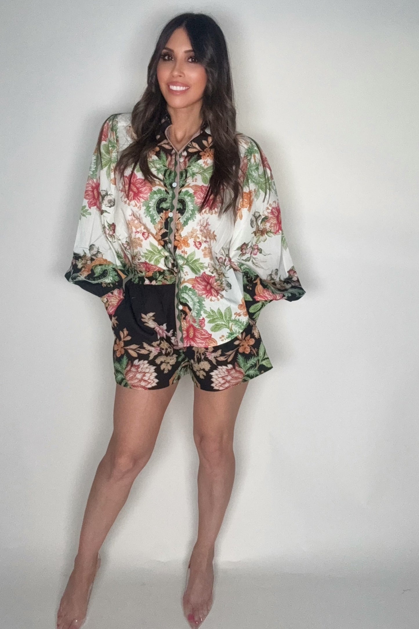 Woman wearing a floral blouse and shorts against a plain background Born To Glam