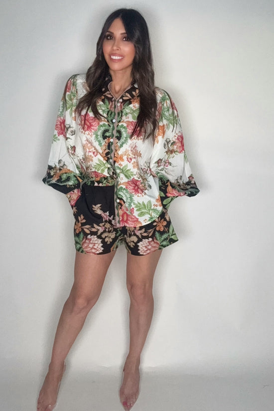 Woman wearing a floral blouse and shorts against a plain background Born To Glam