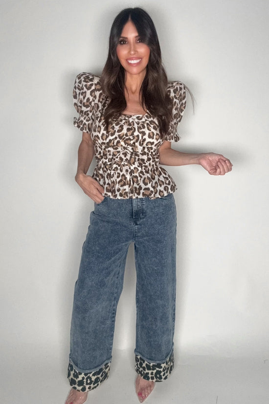 Woman wearing a leopard print top and blue jeans on a plain background Born To Glam