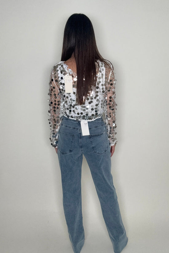 Person wearing a sequin jacket and blue jeans on a plain background Born To Glam