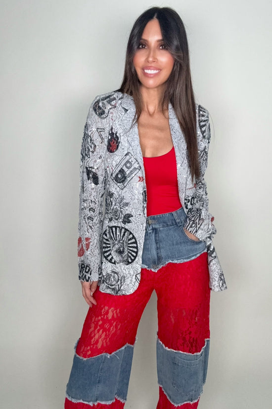 Woman wearing a patterned cardigan, red top, and colorful pants against a plain background Born To Glam
