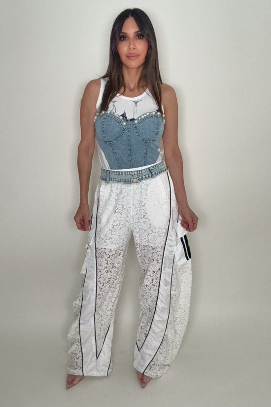 Woman wearing a denim corset top and white pants with black patterns on a plain background Born To Glam