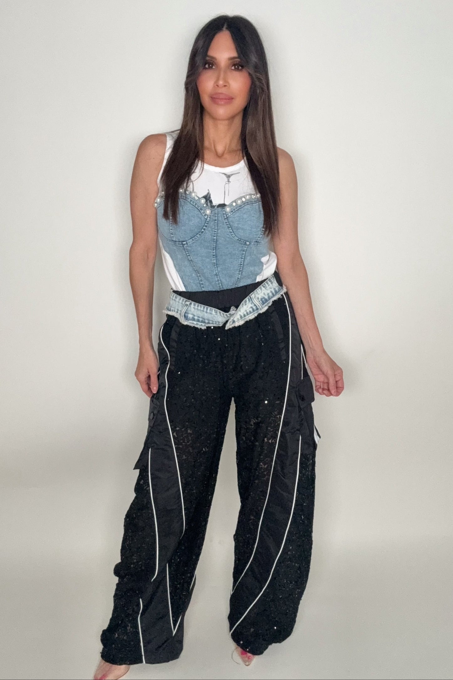 Woman wearing a denim top and black pants with white stripes on a plain background Born To Glam