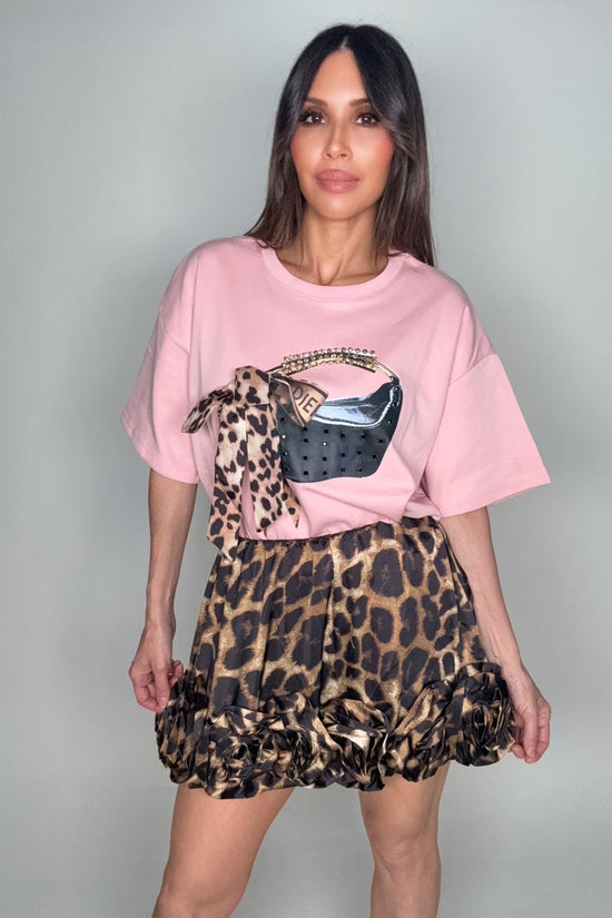 Woman wearing a pink oversized t-shirt with a graphic design and a leopard print skirt on a plain background Born To Glam