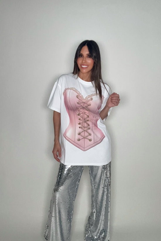 Person wearing a white t-shirt with a pink corset design and silver sequin pants on a plain background Born To Glam