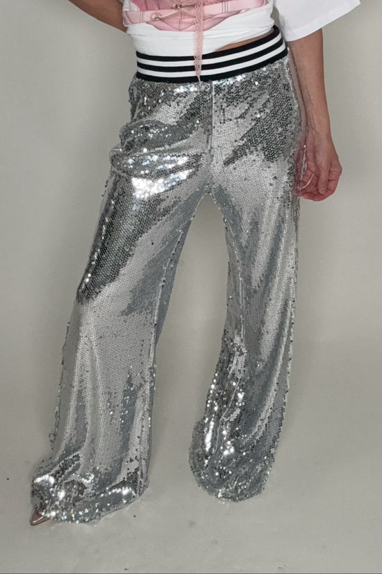 Person wearing a white t-shirt, pink top, and silver sequin pants on a plain background Born To Glam
