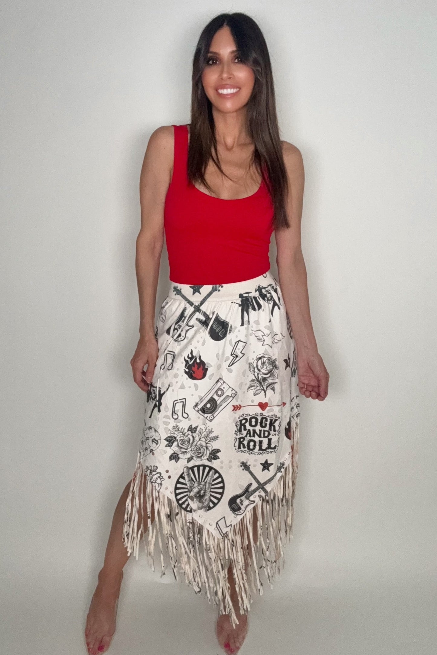 Woman wearing a red top and white skirt with fringe and rock and roll graphics on a plain background Born To Glam
