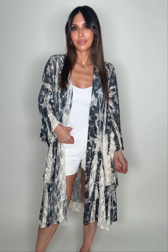 Woman wearing a long, patterned kimono over a white outfit on a plain background Born To Glam