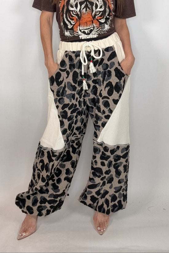 Woman wearing a brown t-shirt with a tiger design and leopard print pants on a white background Born To Glam