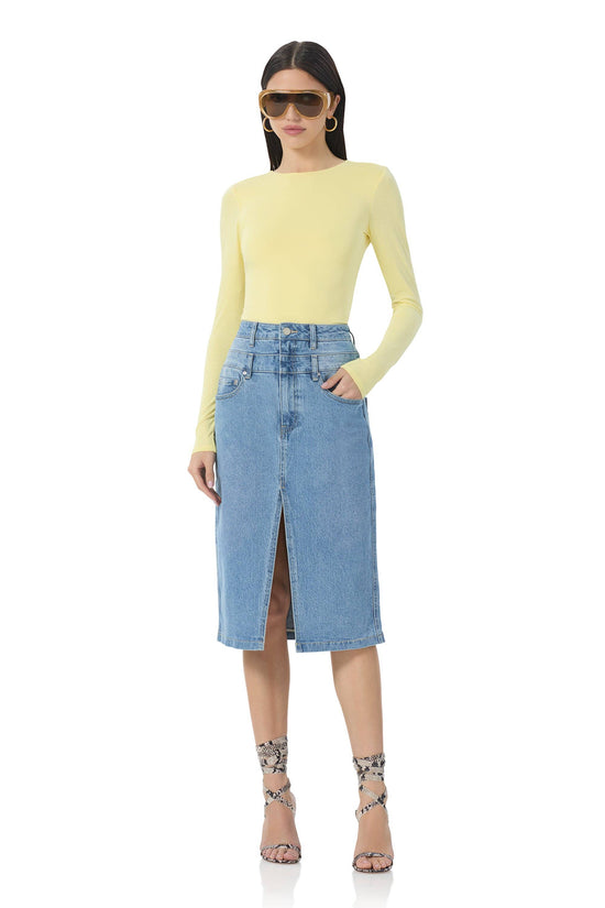 Woman wearing a yellow long-sleeve top and blue denim skirt on a white background Born To Glam
