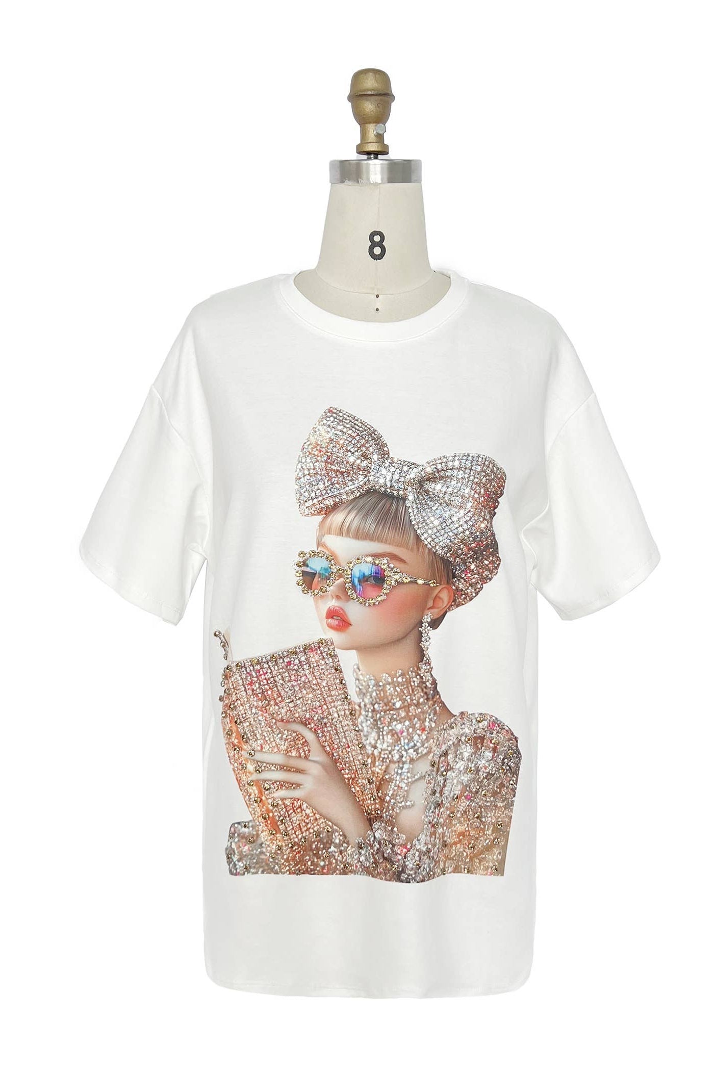 White t-shirt with a graphic of a person wearing sunglasses and a large bow on a mannequin against a white background. Born To Glam