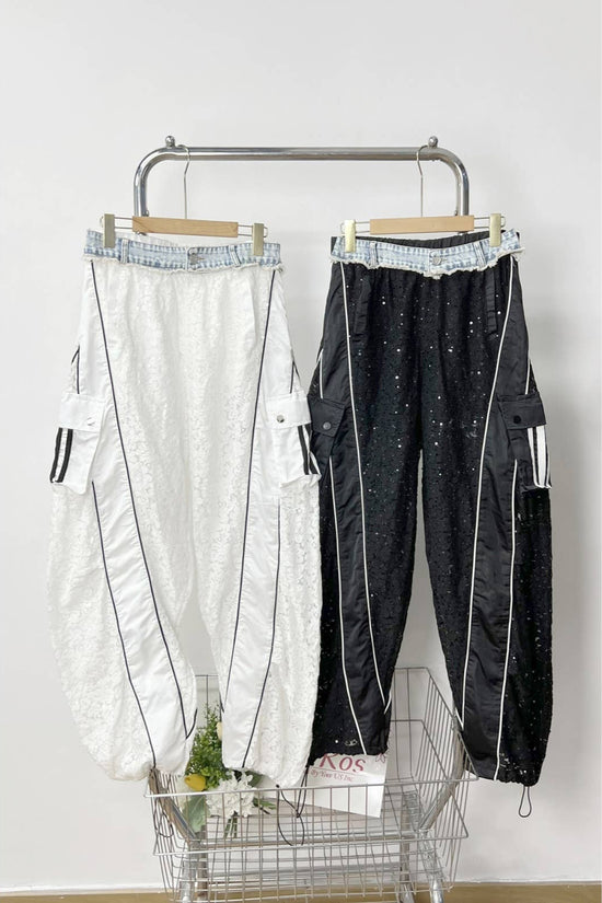 Two pairs of pants hanging on a rack against a white wall. Born To Glam