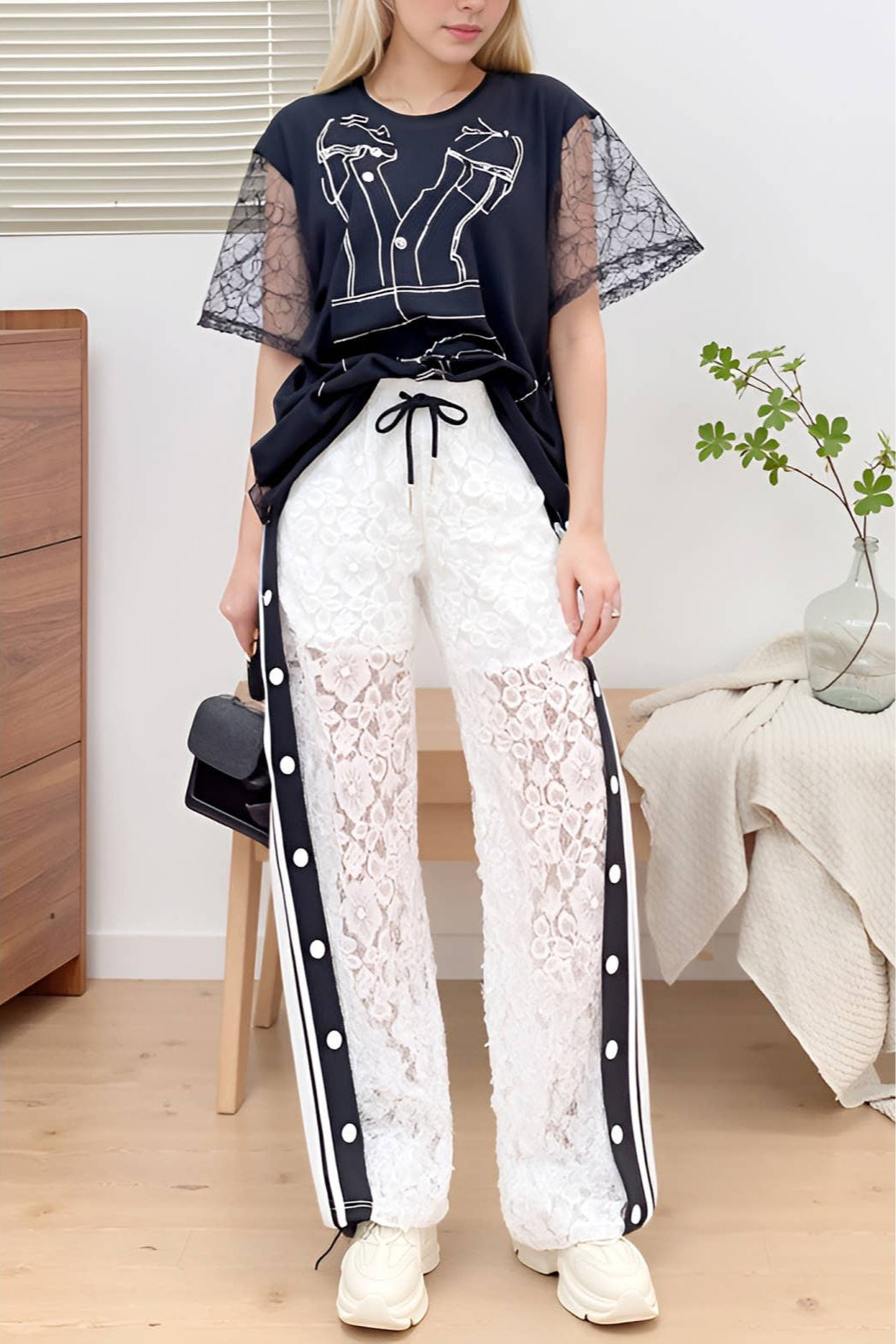 Person wearing a navy top with sheer sleeves and white lace pants in a room setting. Born To Glam