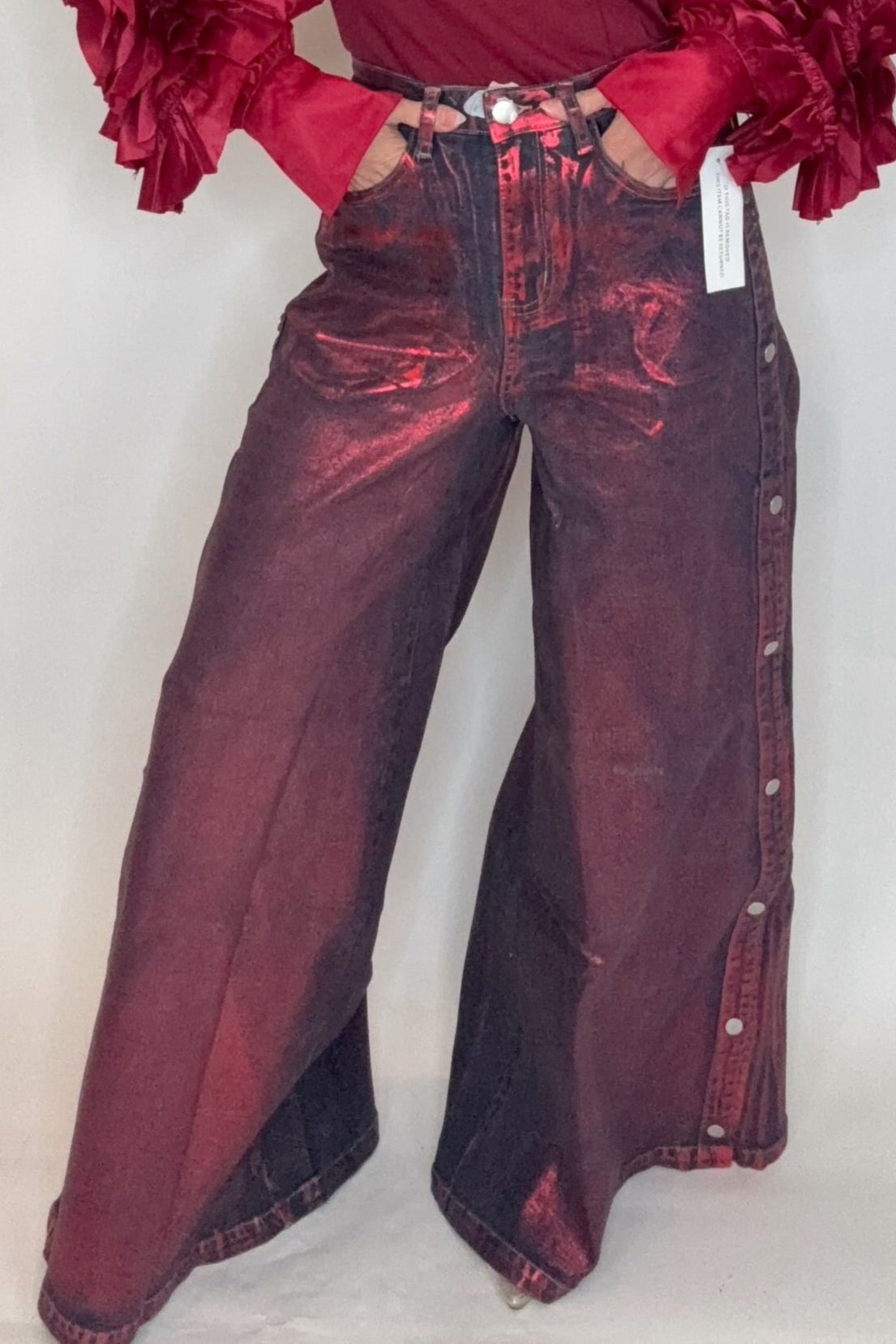 Person wearing a burgundy outfit with ruffled sleeves against a white background Born To Glam